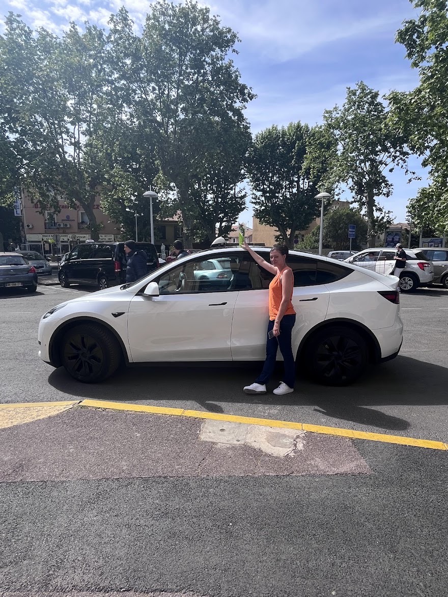 Véro à côté de sa Tesla blanche équipée d’un lumineux taxi.